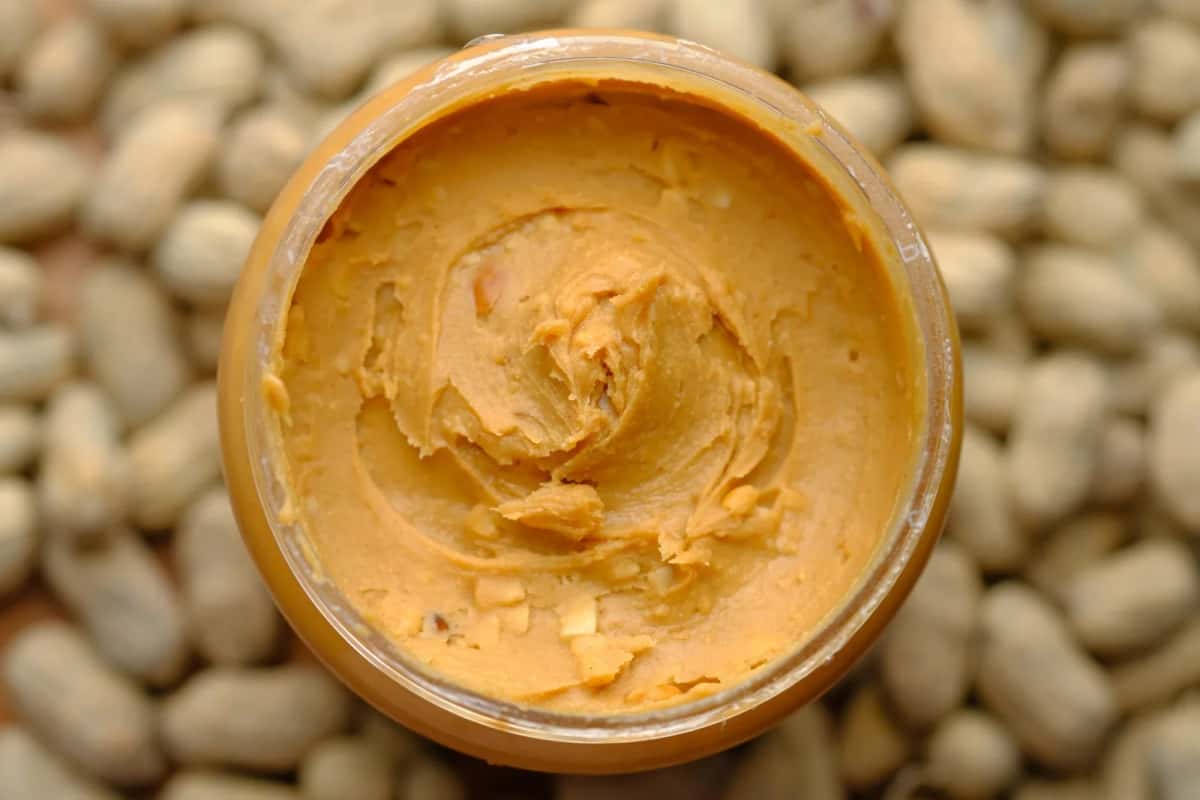 Pot de pâte d'arachide posé sur des cacahuètes décortiquées, base de la sauce du mafé