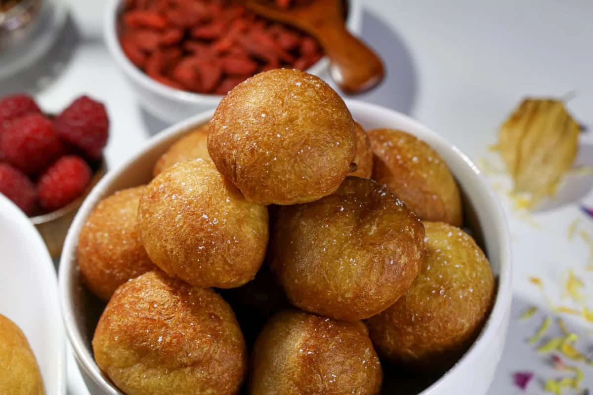 Beignets ronds et dorés saupoudrés de sucre, empilés dans un bol blanc