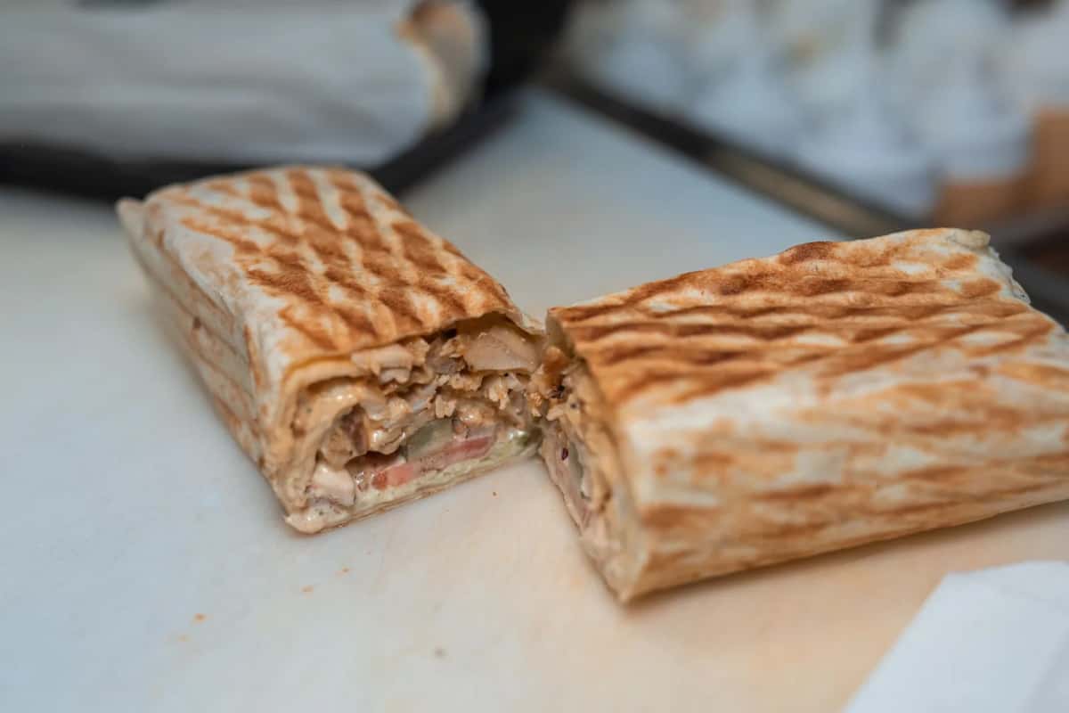 Sandwich chawarma au poulet roulé dans un pain libanais grillé, coupé en deux, avec tomate, cornichon et sauce blanche