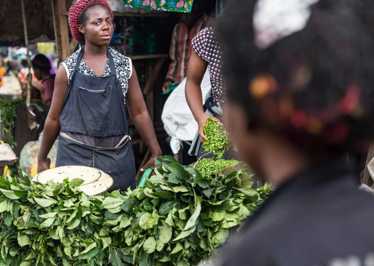 Marchande derrière un étal de feuilles vertes sur un marché d'Afrique de l'Ouest