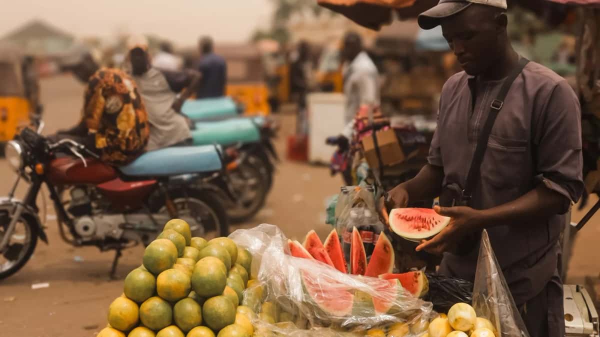 Un vendeur tranche une pastèque devant son étal d'oranges sur un marché de rue