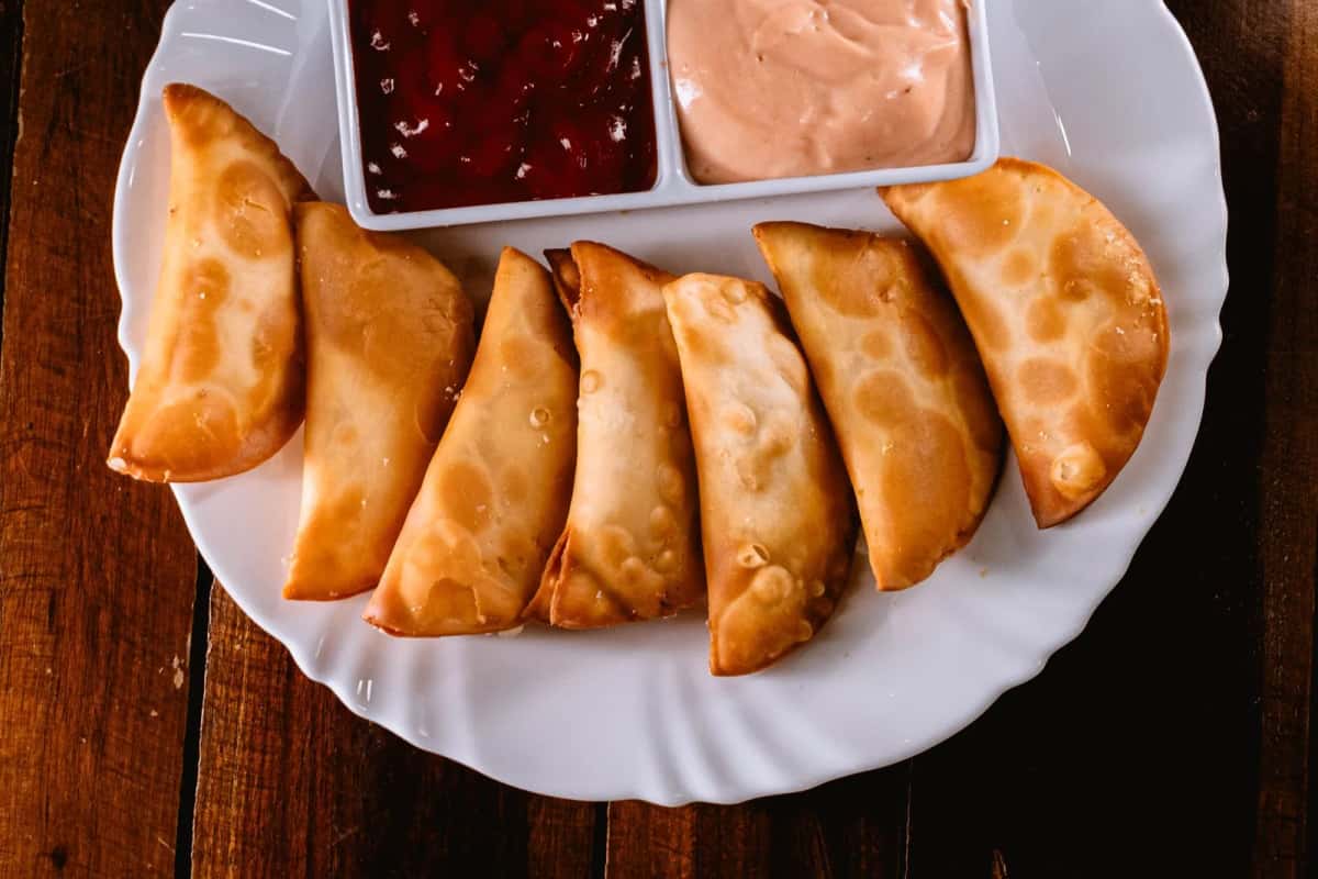 Chaussons frits en demi-lune, dorés, servis sur une assiette avec des sauces à côté