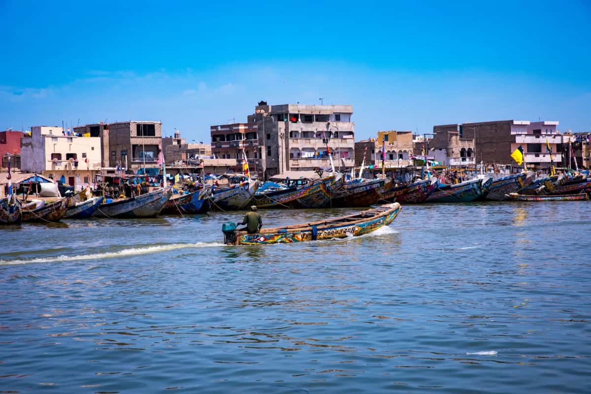 Pirogues de pêche sénégalaises peintes de couleurs vives, amarrées devant des maisons de pêcheurs