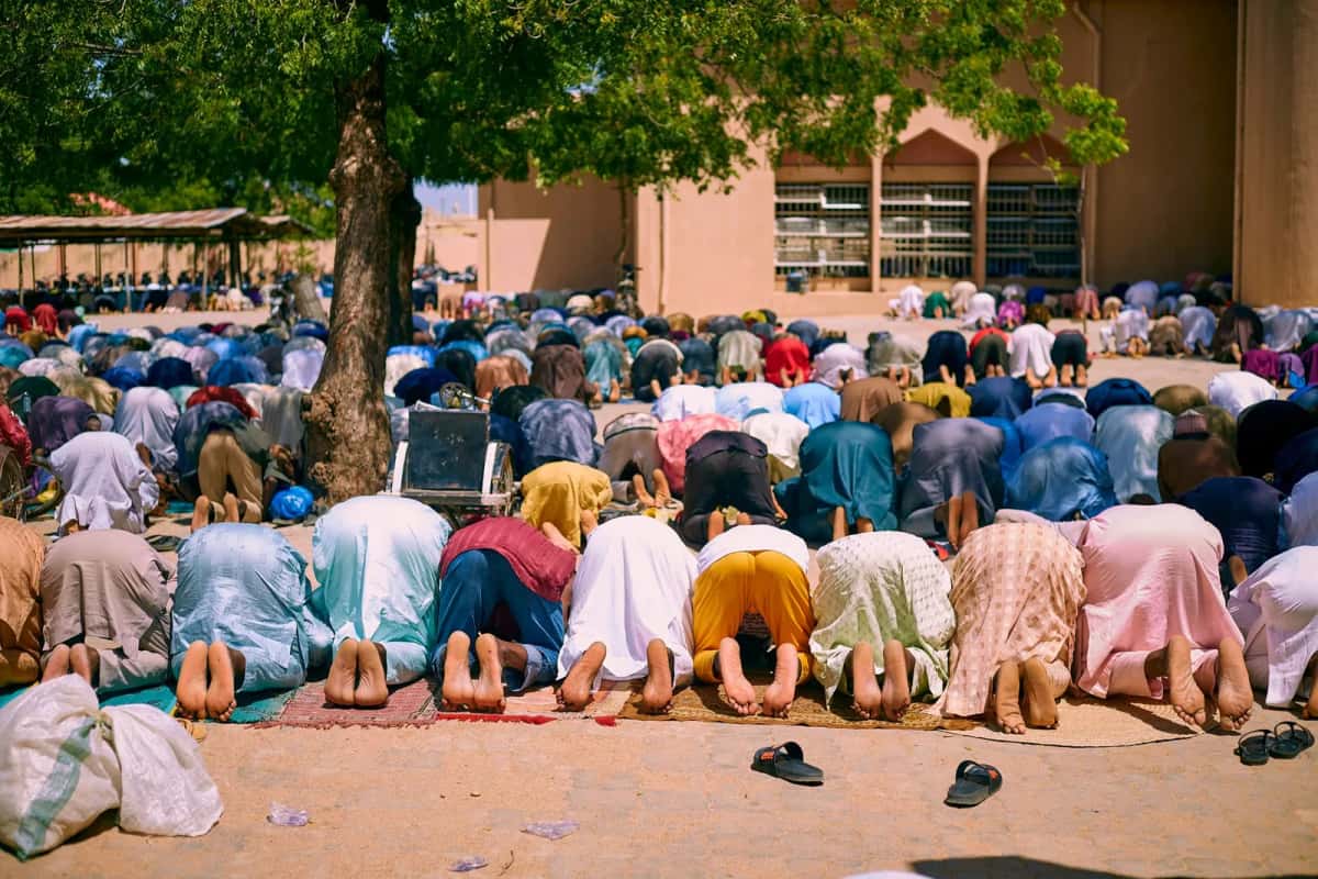 Fidèles en boubous colorés, prosternés sur des tapis pour une prière collective en plein air devant une mosquée