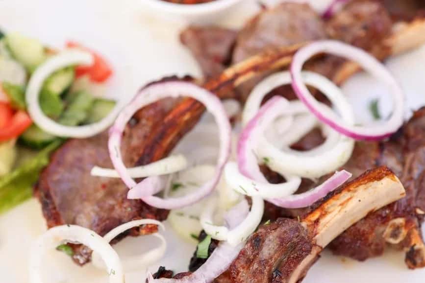 Côtelettes d'agneau grillées garnies d'oignons rouges et blancs, avec une salade de concombre et de tomate