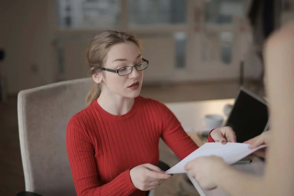 Employée de bureau recevant un dossier papier tendu par un usager à l'accueil