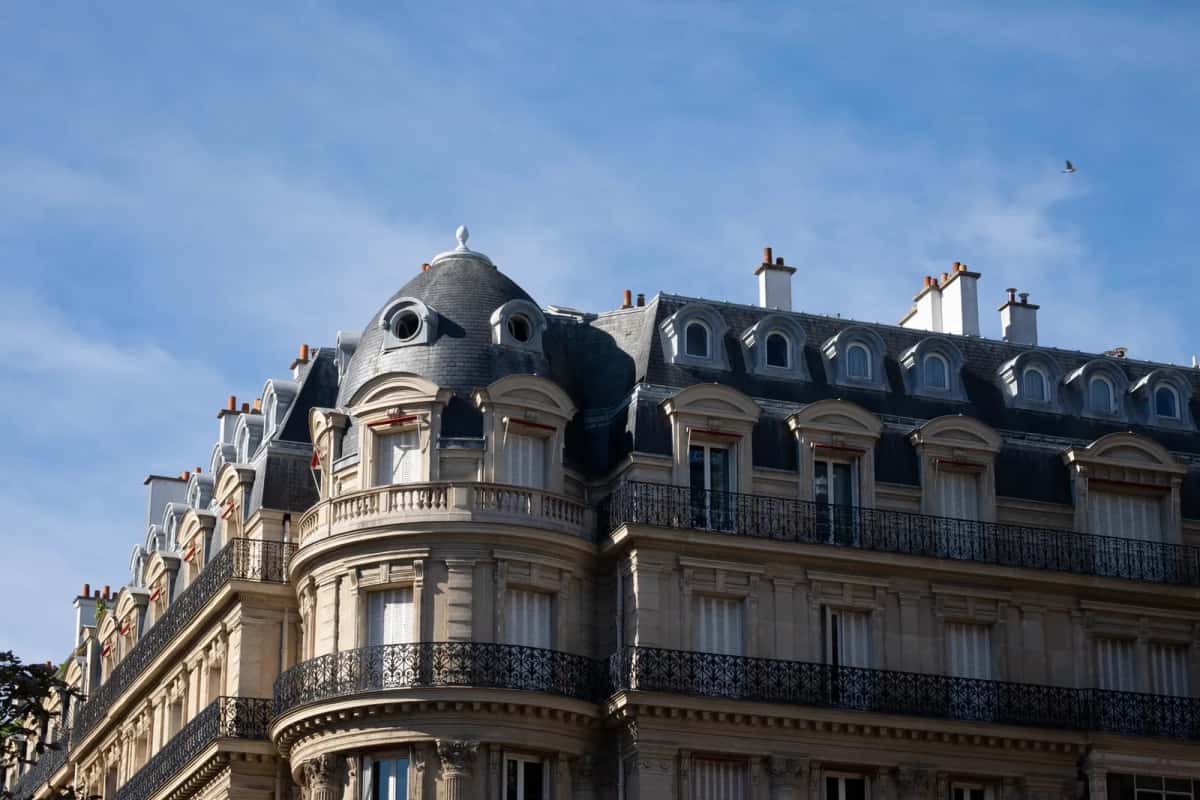 Façade d'immeuble haussmannien parisien avec balcons en fer forgé et toits en zinc