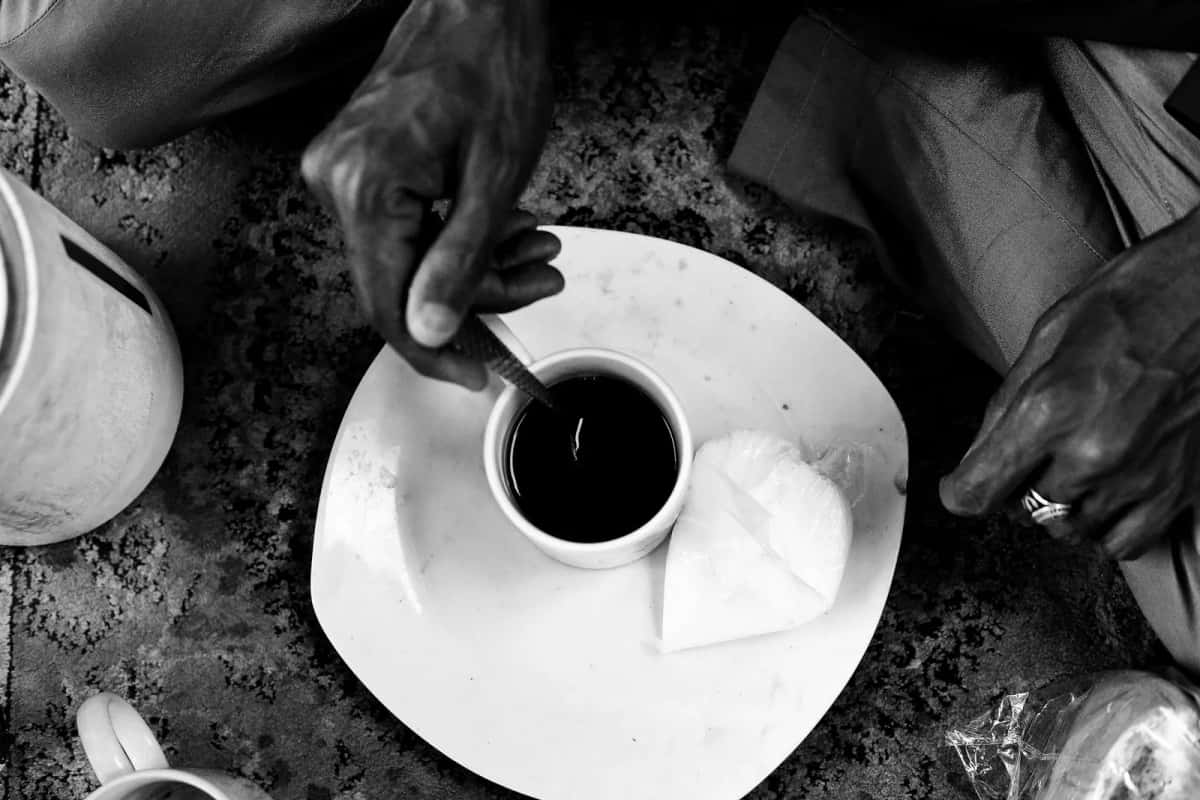 Tasse de café noir qu'un homme remue avec une cuillère, en noir et blanc