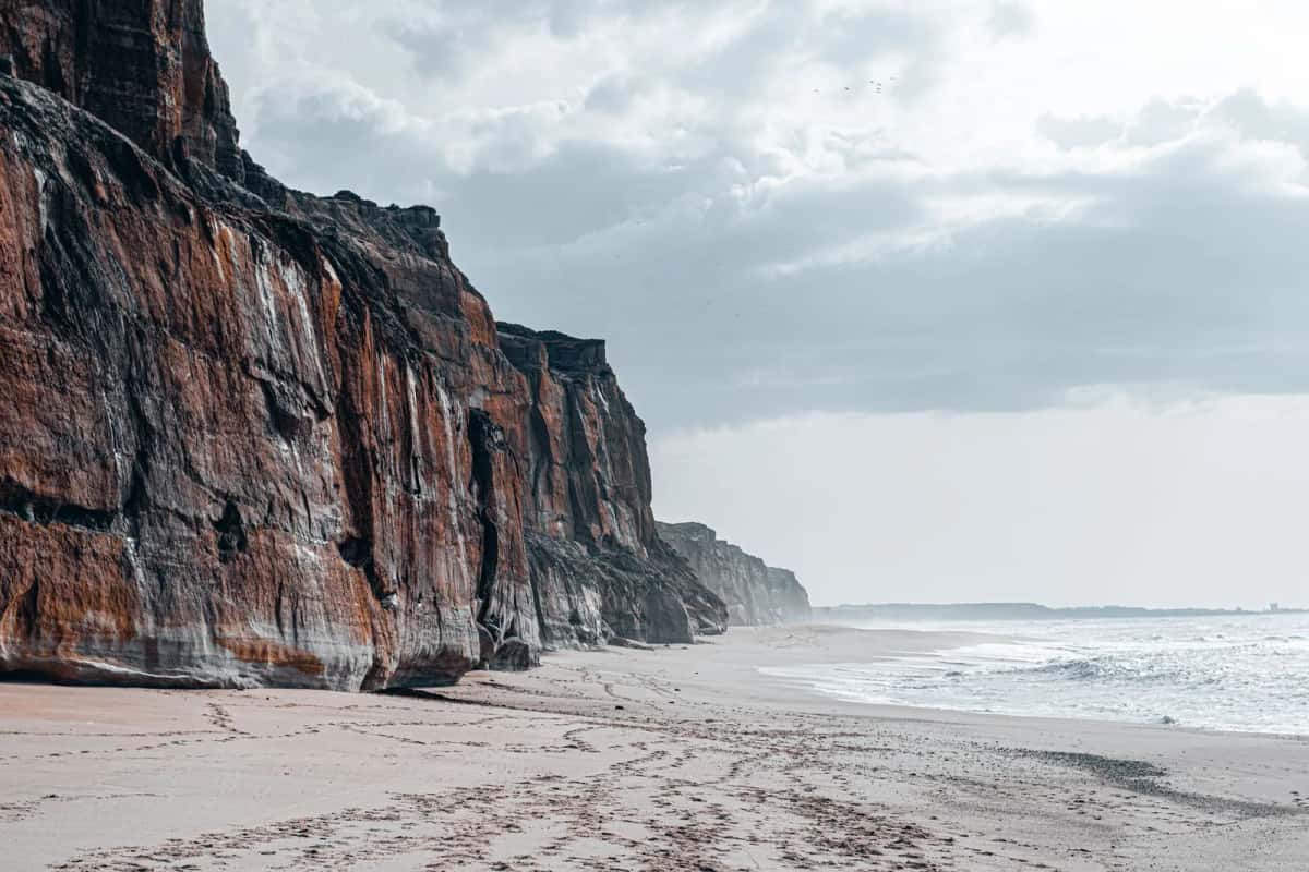 Haute falaise de roche ocre dominant une longue plage de sable clair