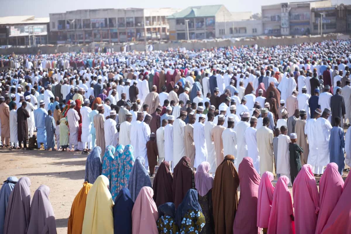 Foule de fidèles en prière en plein air, hommes en boubous et femmes en voiles colorés