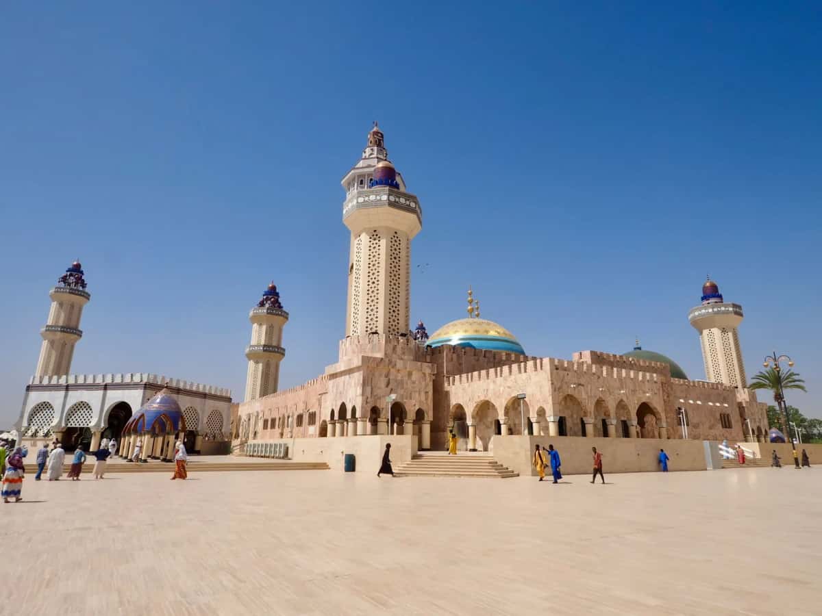 Grande mosquée sénégalaise aux minarets et dômes dorés et bleus, sur une vaste esplanade sous un ciel bleu