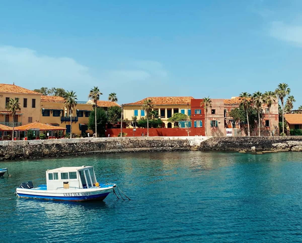 Maisons coloniales ocre et rouges du front de mer de l'île de Gorée, avec une barque blanche au premier plan