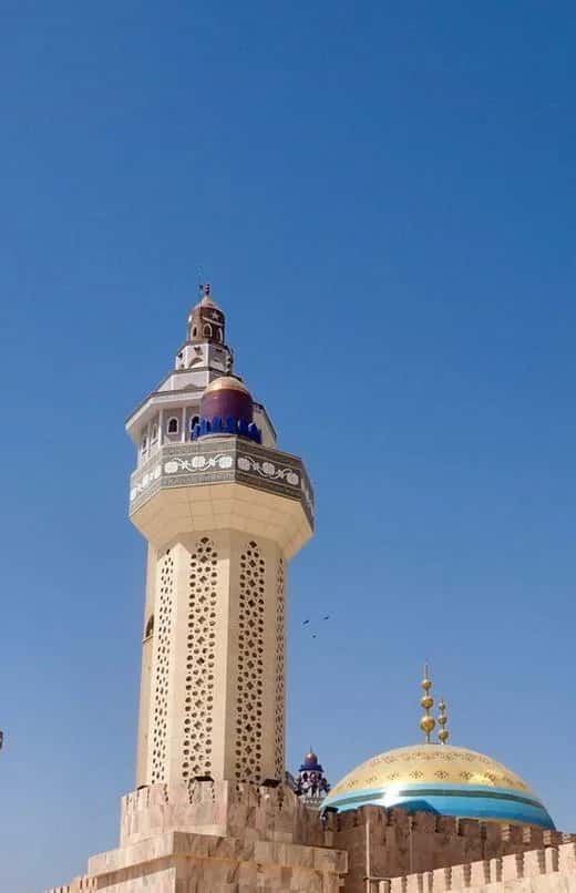 Minaret ajouré d'une grande mosquée sénégalaise, près d'un dôme doré, sous un ciel bleu