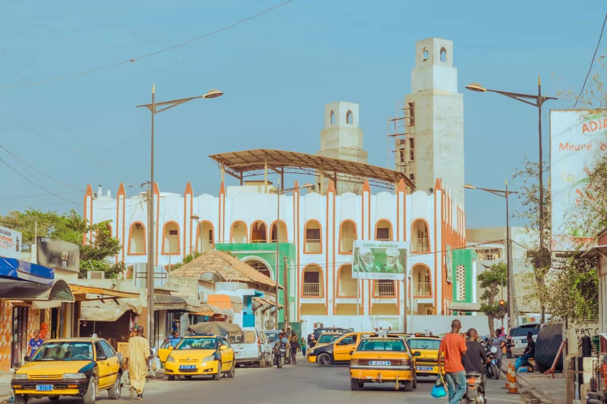 Rue animée du centre de Dakar avec taxis jaunes, minarets et façade blanche à arcades