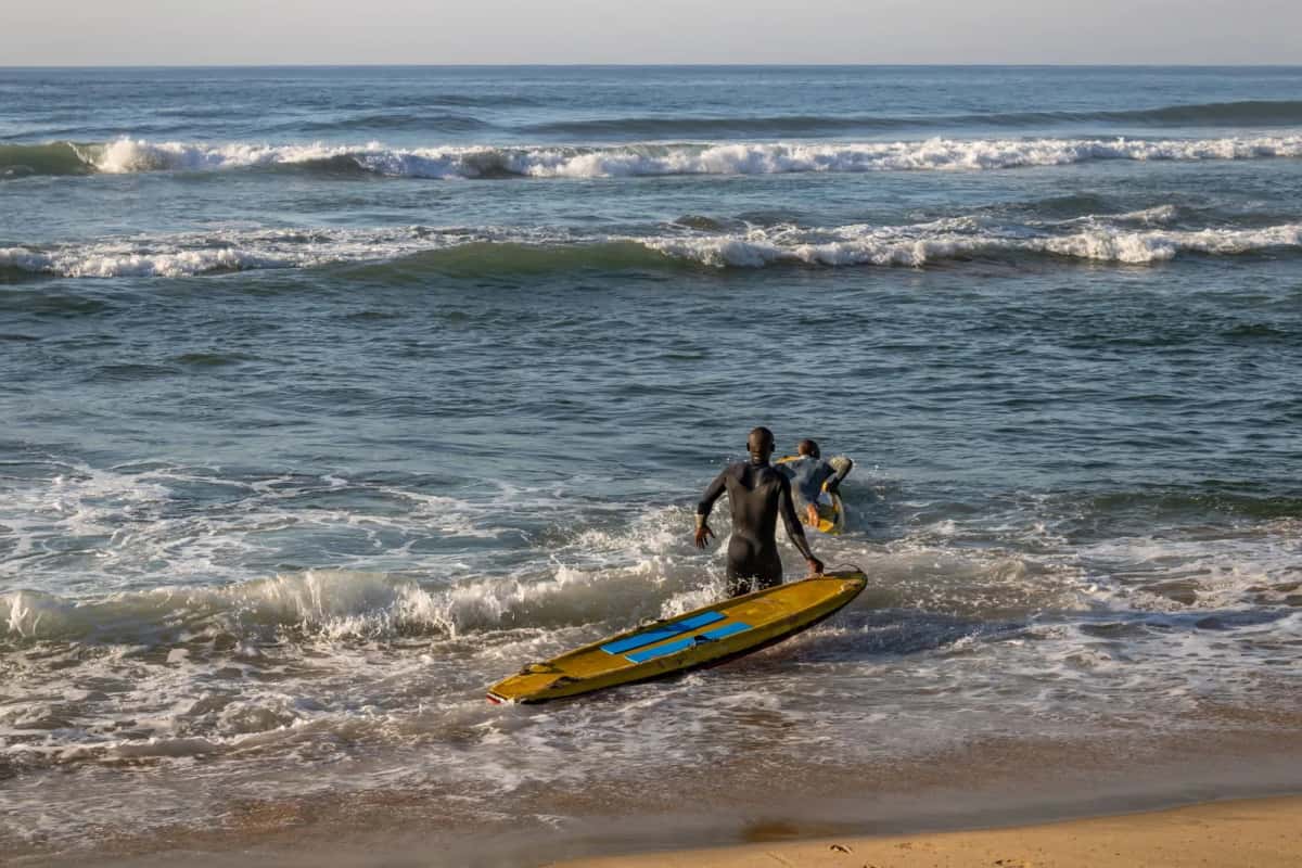 Surfeur sortant de l'eau avec une planche jaune sur une plage battue par les vagues