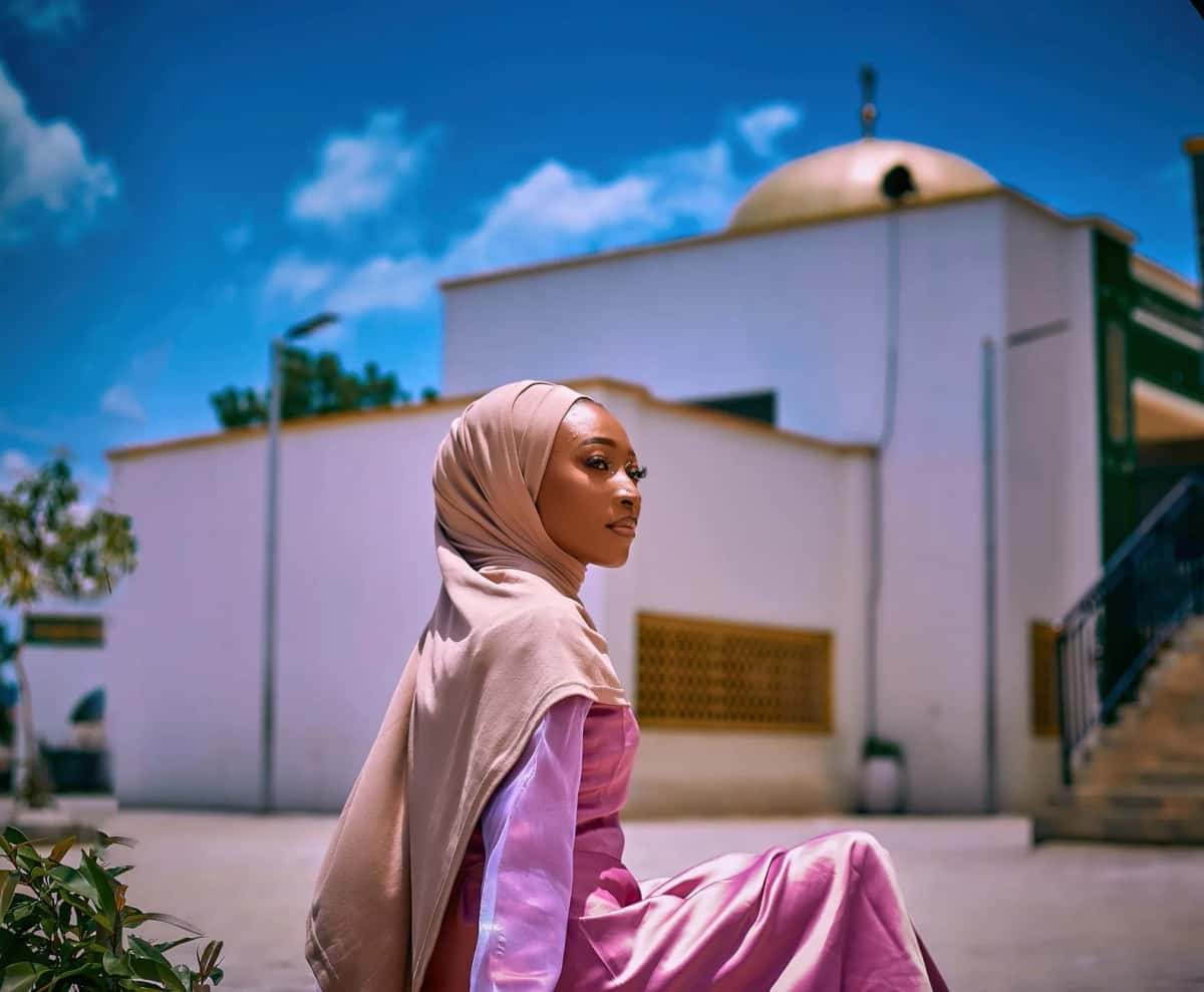 Femme portant un foulard et une tenue à manches longues devant une mosquée en Afrique de l'Ouest